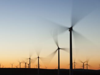 Wind turbines in front of a sunrise, with their blades blurred due to their motion.
