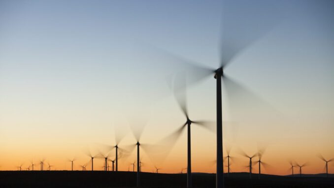 Why wind farms attract so much misinformation and conspiracy theory Wind turbines in front of a sunrise, with their blades blurred due to their motion.