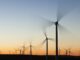 Wind turbines in front of a sunrise, with their blades blurred due to their motion.